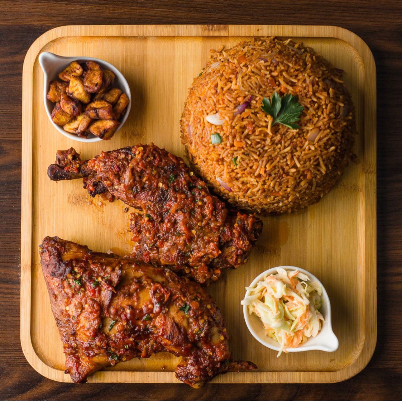 Grilled chicken platter with jollof, plantain and coleslaw on a wooden board