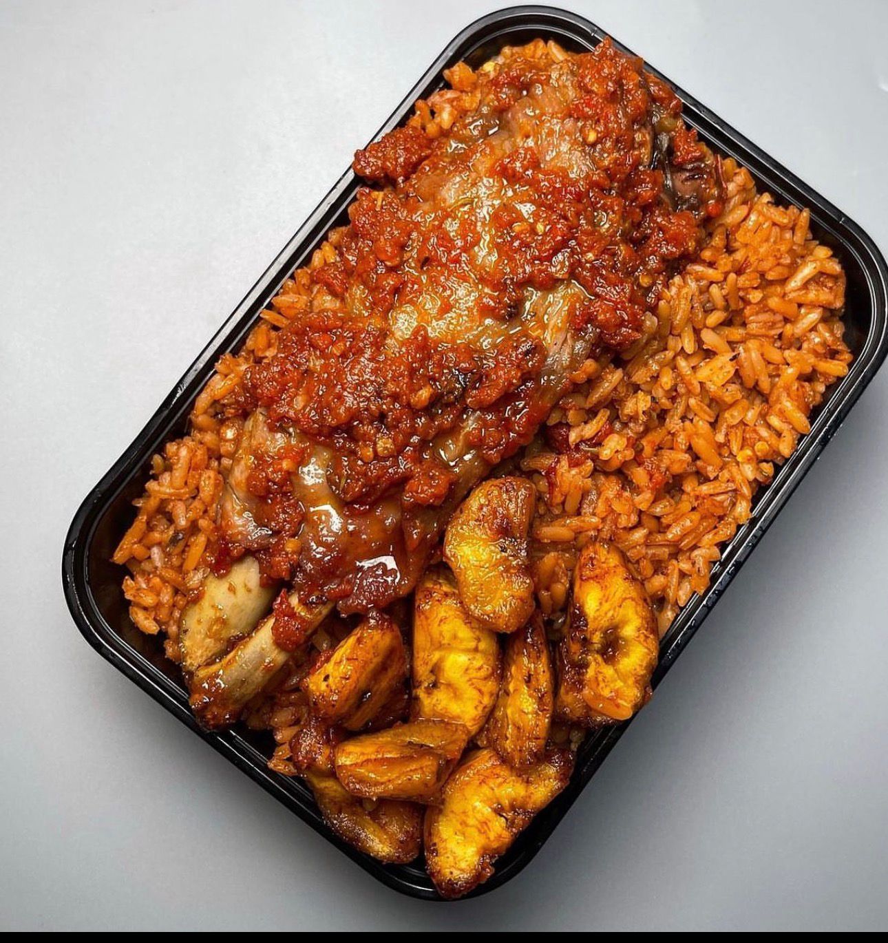 Jollof rice with chicken and fried plantain in a takeaway box